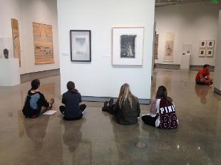 Hope College students studying artworks while seated on the floor of the Kruizenga Art Museum's gallery space.